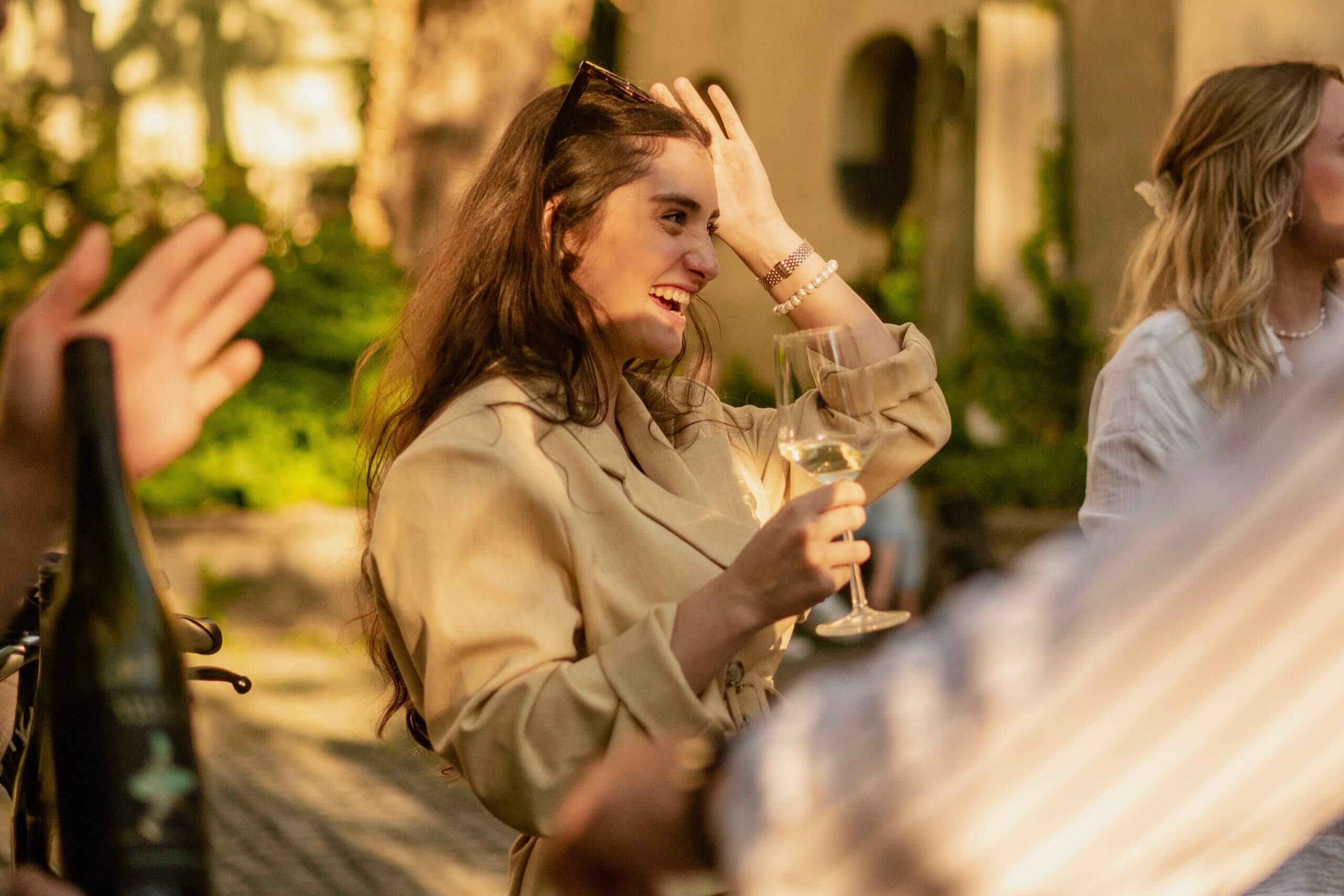 female laughing with wine glas in hand an sunglases on head outdoor